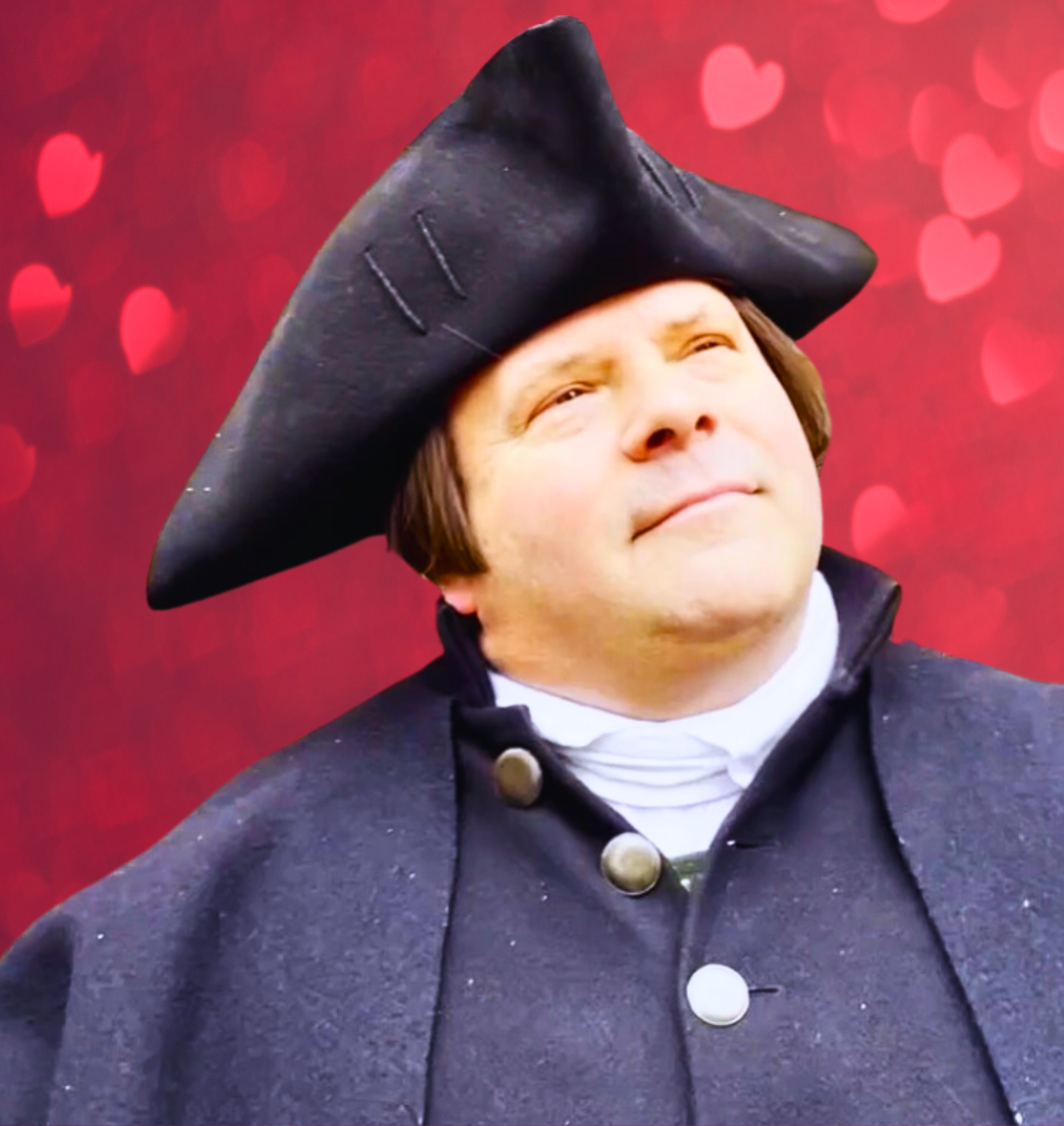 A Paul Revere reenactor in front of a red background with hearts. 