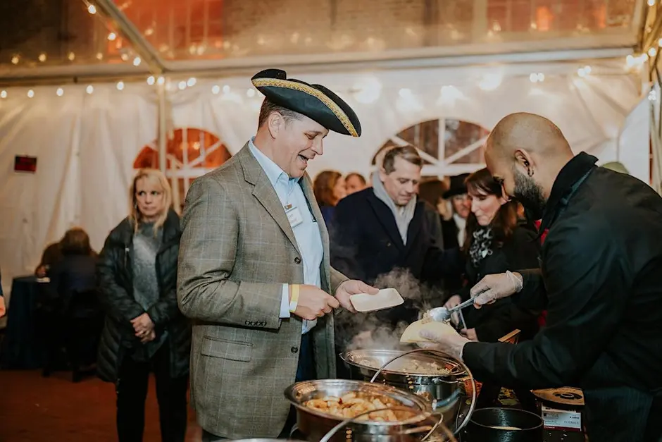 A guest in a tricorn hat enjoying food at Lanterns & Luminaries