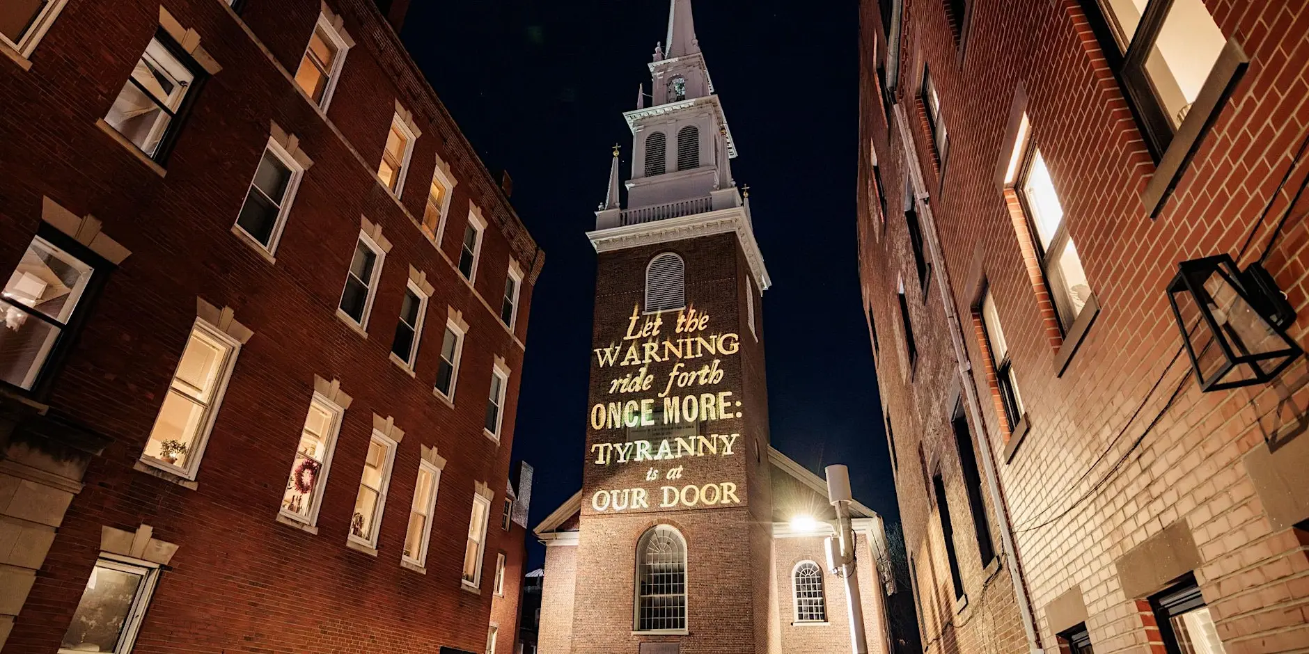A projection onto the Old North Church by Silence Dogood that reads: "Let the Warning ride forth Once More Tyranny is at our Door."